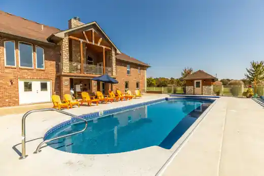 Pool beside a brick lake home with a surrounding deck