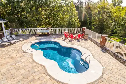 Freeform pool with a paver patio and a white fence