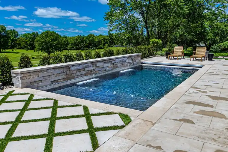 Rectangular pool with a stone sheer-descent wall and grass pavers