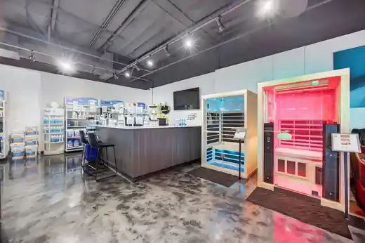 A pool supply counter with chemical shelves beside two display saunas, one lit pink